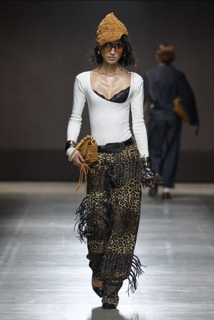 Female model walking down the runway with a scoop-neck top and printed pants.