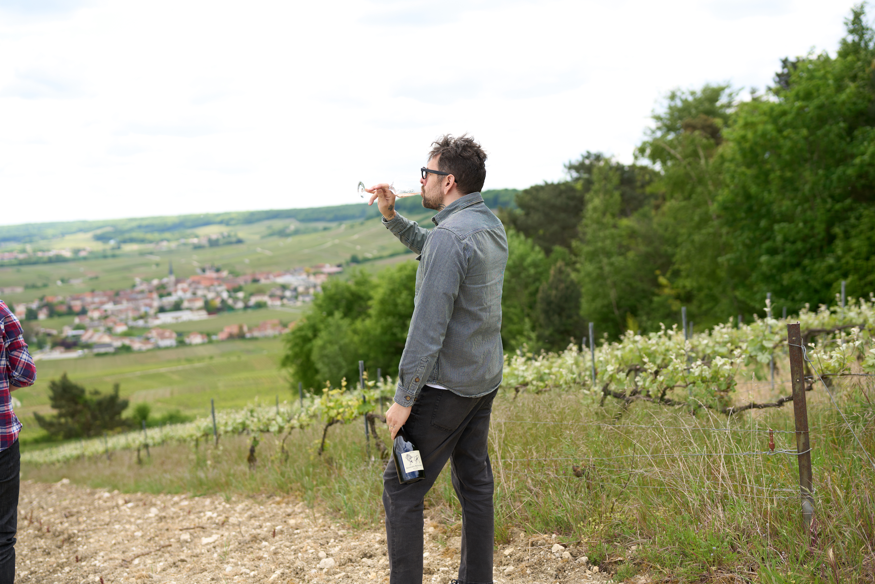 Sommelier Kyle Paton standing in a vineyard, drinking a glass of wine.
