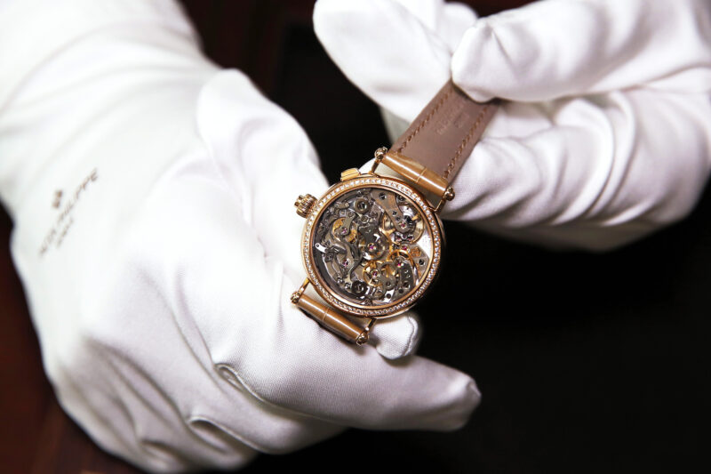 Close up of hands wearing white gloves holding an intricate luxury gold watch.