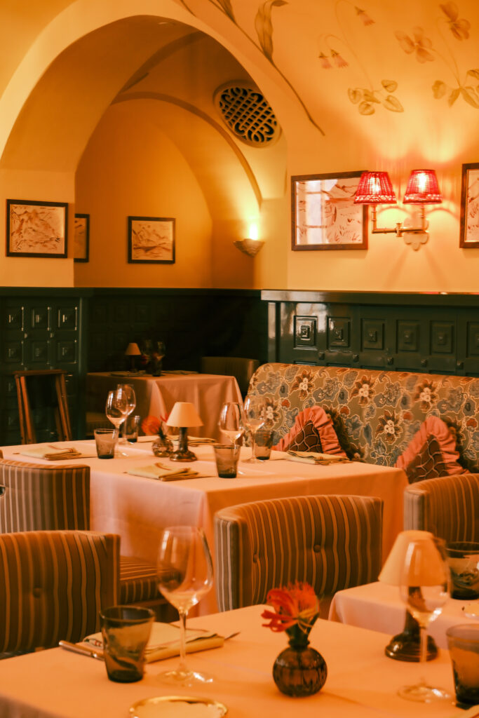 A restaurant filled with warm lighting, elegant dinning tables and floral accent seating.